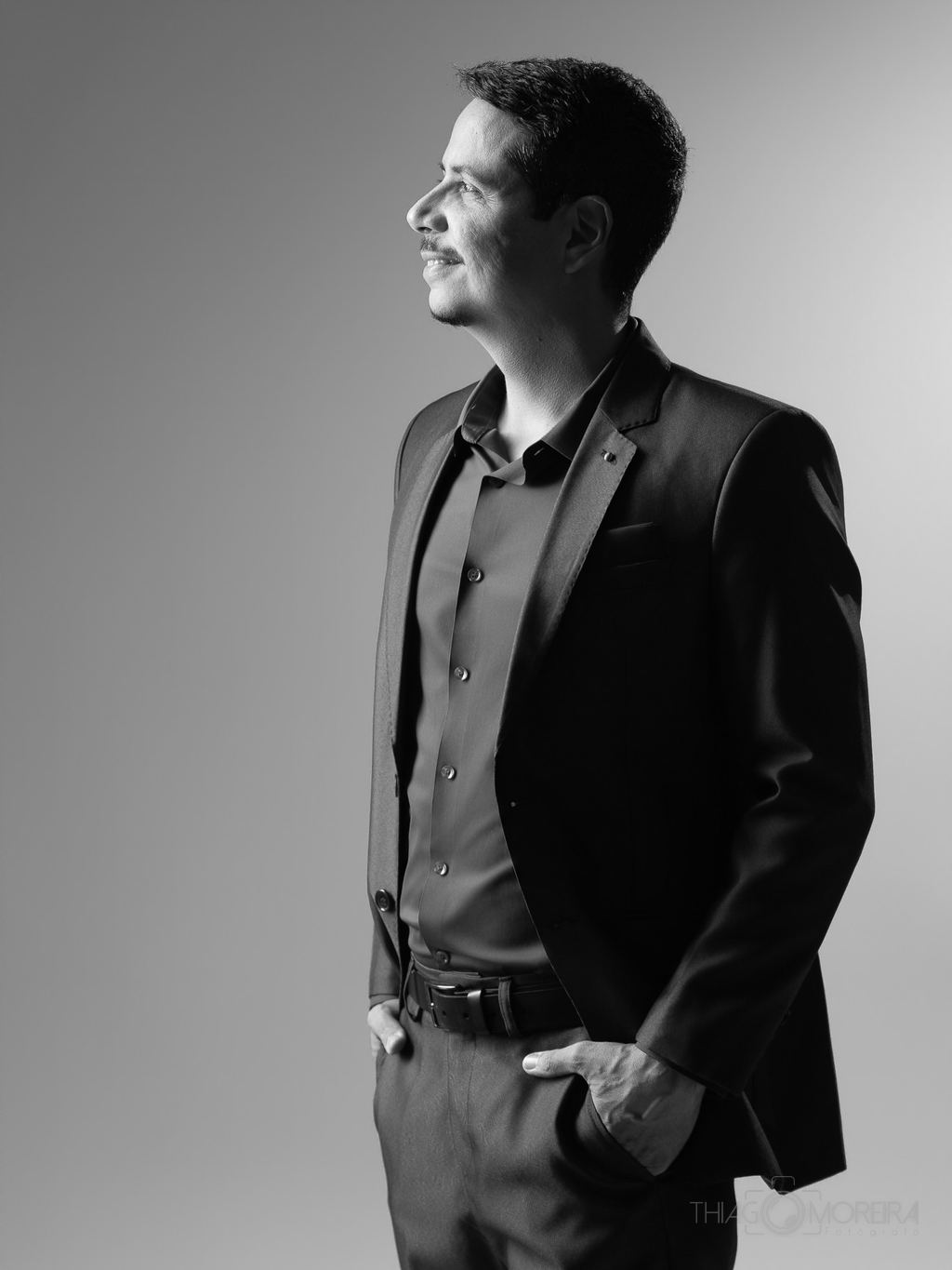 Retrato corporativo em preto e branco de um homem de terno, de perfil, com luz lateral marcando o contorno do rosto